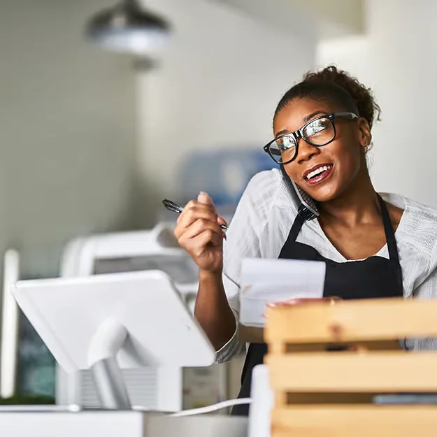 A small business owner on the phone at her shop counter, beside a card terminal and till