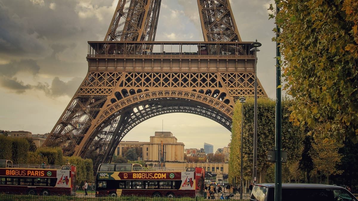 Open-top sightseeing tour buses passing beneath the Eiffel Tower in Paris