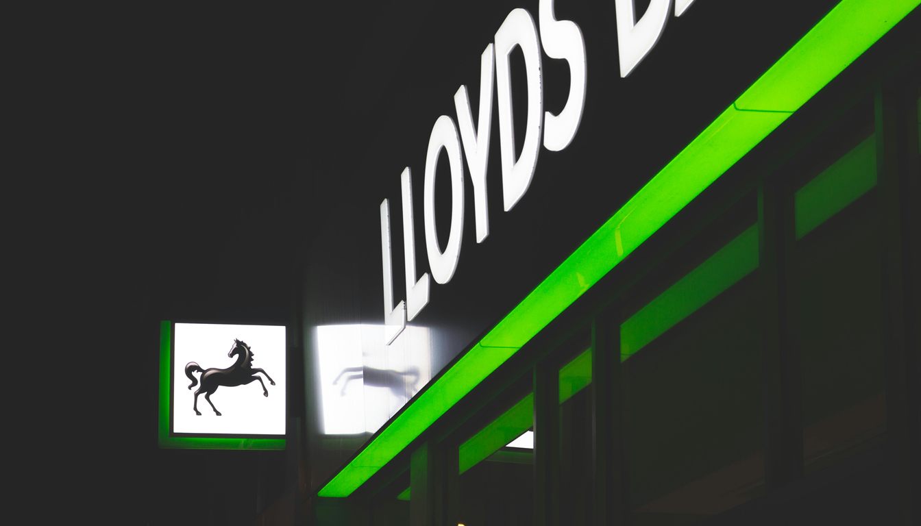 An illuminated Lloyds Bank branch sign with its black horse logo lit up at night on a UK high street